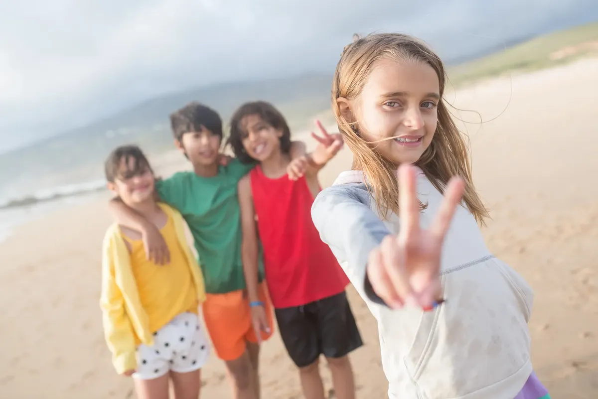 Group of kids having fun on a beach in Portugal, smiling and making peace signs.